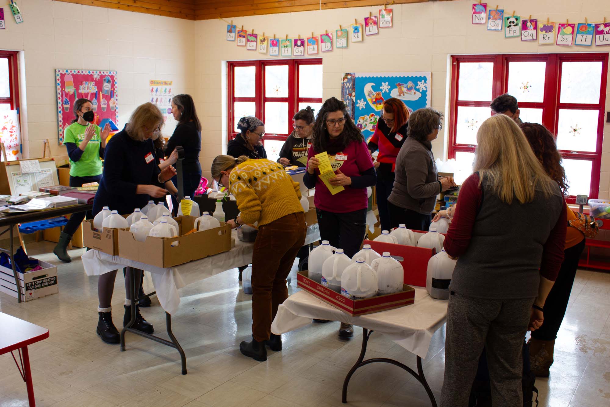 a group of people working around folding tables of milk jugs being filled with dirt and seeds