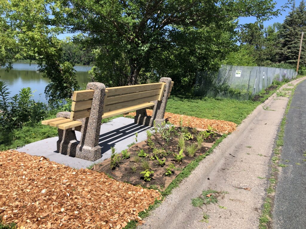 A new wood and cement bench with cedar chips and freshly planted seedlings next to the fenced garden area.